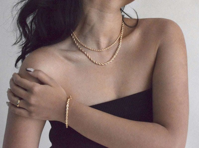 woman wearing gold jewelry and layering gold rope necklaces together
